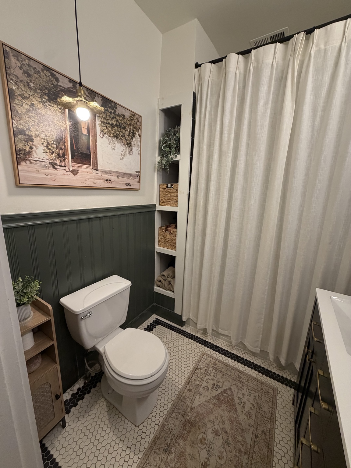 Finished upstairs bathroom with deep green beadboard, built-in shelving, and a linen shower curtain