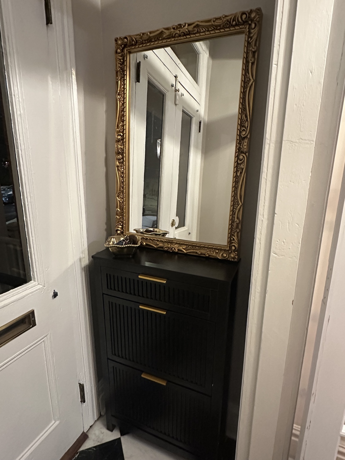 Black shoe cabinet and ornate gold mirror in the finished front vestibule
